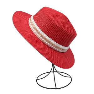 Detail of red straw sun hat featuring a pearl and gold chain decorative band
