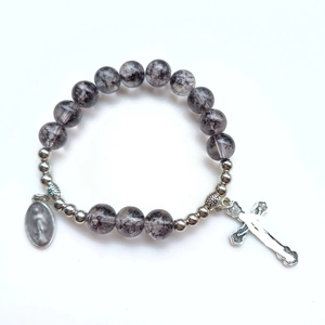 Dettaglio del bracciale in perle di vetro marmorizzato grigio con croce e medaglia d'argento