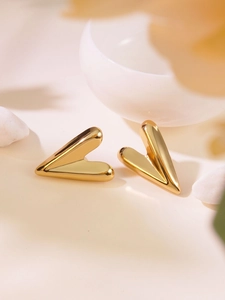 Detailed view of polished golden heart-shaped stud earrings on a ceramic dish background