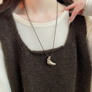 Detail of golden croissant pendant with leather cord worn over white and brown knitwear