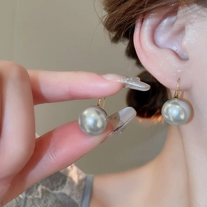 Close-up of elegant 18K gold hook earrings with round silver-grey pearls and metallic luster