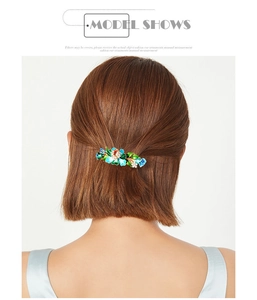 Detail of floral enamel spring hair clip with rhinestones worn on brown wavy hair