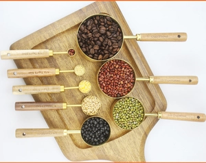 Flat lay of 8-piece gold stainless steel measuring cups and spoons with acacia wood handles