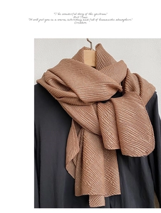 Dettaglio di una sciarpa marrone con texture stropicciata su abiti neri per un look invernale