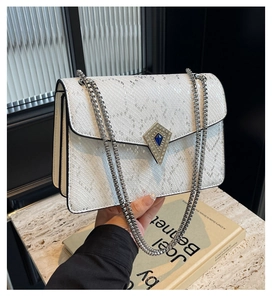 Detail of white snake-embossed bag featuring a jewel-encrusted lock and silver chain