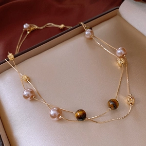 Detail of layered gold necklace with pink pearls and tiger eye beads on velvet
