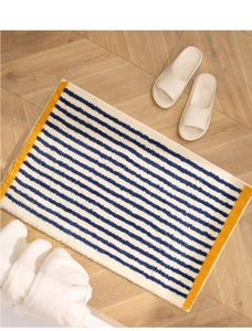 Close-up of rectangular plush beige bath mat with blue stripes and yellow borders on wood