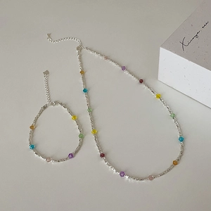Macro view of minimalist silver beaded necklace and bracelet with colorful crystals