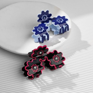 Floral resin hair clips with rhinestone centers in blue and black colors on a white tray