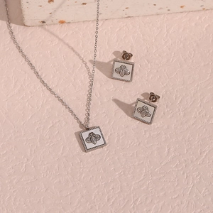 Detailed view of silver square shell bee pendant necklace and earring set on stone