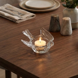 Minimalist transparent glass bird candle holder with a lit tealight on a wooden table