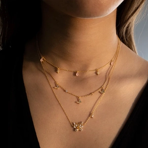 Detailed close-up of a three-layer gold butterfly necklace with pink charms and crystals