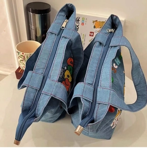 Close-up of two blue denim handbags featuring colorful embroidery and secure zip closure