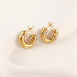 Golden C-shaped hoop earrings with sparkling cubic zirconia on a white wavy plate