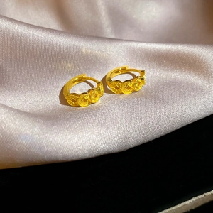 Close-up of 18k gold plated coin-shaped earrings resting on elegant champagne silk fabric