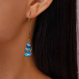 Gros plan de boucles d'oreilles bohèmes en pierres marbrées bleues portées par un mannequin