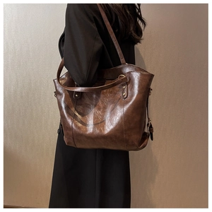 Detail of a large dark brown PU leather tote bag with shoulder straps and metal rings