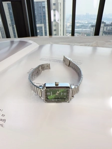 Close-up of square green dial watch with silver metal bamboo link strap on magazine