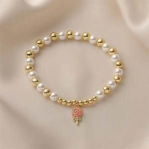 Close-up of pearl and gold bead bracelet featuring a pink enamel lollipop charm detail