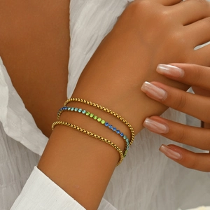 Close-up of stacked gold bead bracelets and gradient blue zircon tennis bracelet