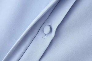 Macro detail of light blue woven fabric and matching fabric-covered button on shirt