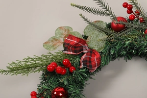 Close-up of artificial Christmas wreath with red berries, pine needles and a plaid bow
