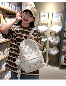 Detailed view of white strawberry pattern backpack with a cute plush charm accessory