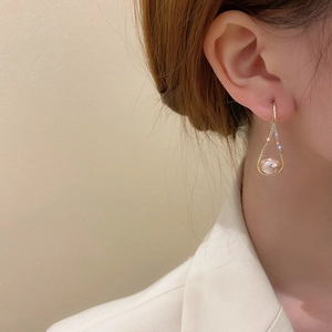 Close-up of gold hollow teardrop earrings with crystals and pearl on female model