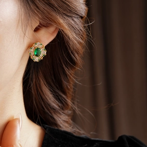 Gros plan d'une boucle d'oreille vintage avec pierre verte et zircons sur l'oreille