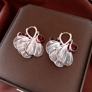 Elegant rose gold hollow petal earrings with ruby red drop stones on leather box