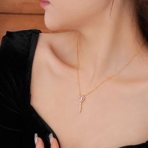 Close-up of golden key necklace with pink heart zircon and white stones on neck