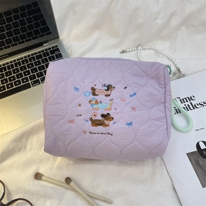 Close-up of quilted lavender cosmetic bag featuring embroidered cartoon dogs and a green strap