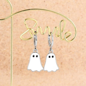 Detail of cute white ghost enamel earrings hanging on a gold metal display stand