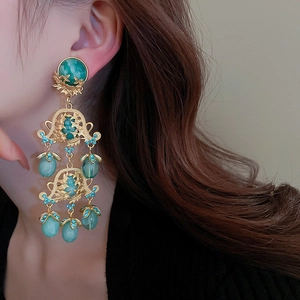 Détail de boucles d'oreilles baroques dorées avec résine verte et cristaux fins
