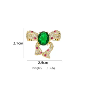 Detail view of a gold bow brooch with a large green emerald and pink stones, 2.5cm size