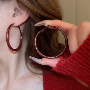 Detailed view of large deep red enamel hoop earring worn with matching red knit sweater
