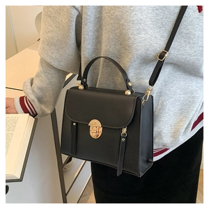 Detail of elegant black crossbody bag featuring a golden round buckle and soft PU texture