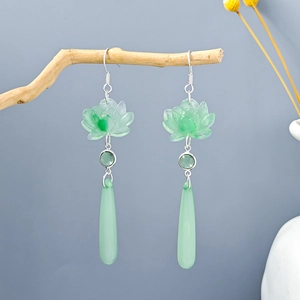Detail of light green lotus petal earrings with long teardrop pendant on wooden branch