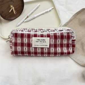 Detail of red checkered storage bag with white lace trim and cloth label on wooden desk