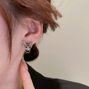 Macro shot of a silver cat head earring with dark gems and a delicate hanging chain