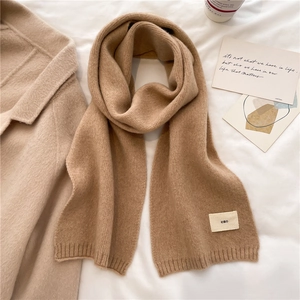 Flat lay of camel knit scarf with emo label next to coffee and beige coat on white fabric