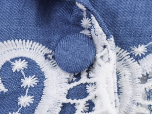 Macro detail of blue woven fabric with white embroidery and matching cloth button