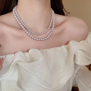 Close-up of double-layer pearl necklace on model wearing white off-shoulder top