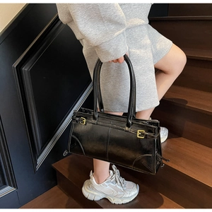 Close-up of black patent leather tote bag with gold hardware on wooden stairs