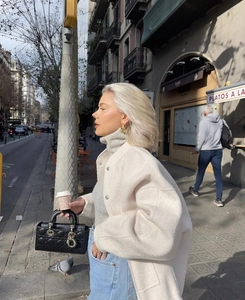 Street style view of a cream loose jacket paired with a black quilted handbag and denim
