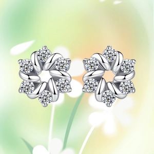 Macro shot of silver flower earrings with clear zircon petals on a soft green background