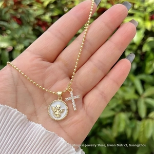 Dettaglio collana a sfere oro 18K con medaglione angelo e pendente a croce in zirconi
