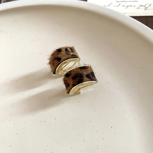 Macro shot of gold C-shaped leopard print earrings on a beige ceramic jewelry tray