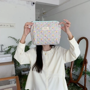 Quilted floral makeup bag with light blue zipper and beige woven label held by a person