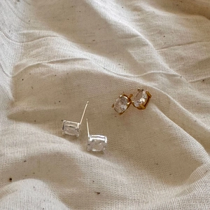Macro view of gold and silver rectangle cut stud earrings on soft linen fabric